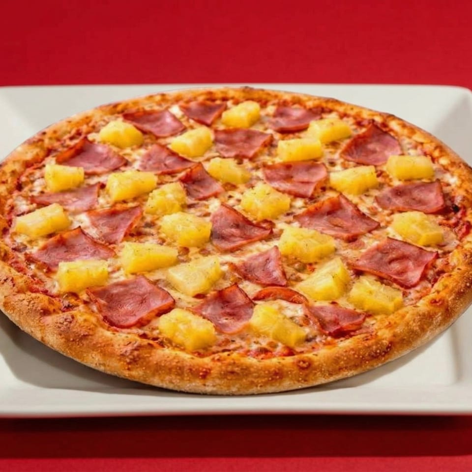 Hawaiian pizza with ham and pineapple on a white plate against a red background.
